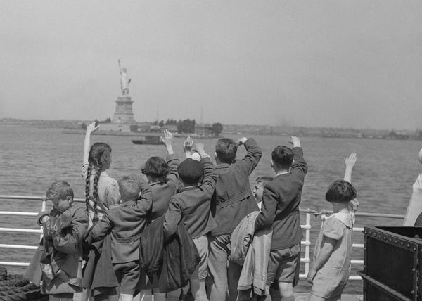 Black and white photo of children waving at Ellis Island from a boat